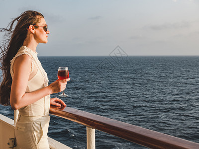 时髦红酒杯户外在蓝色海浪的背景下在游轮的露天甲板上拿着一杯漂亮的粉红葡萄酒时尚女人侧视图特写休闲和旅行的概念女人拿着一杯漂亮的粉图片