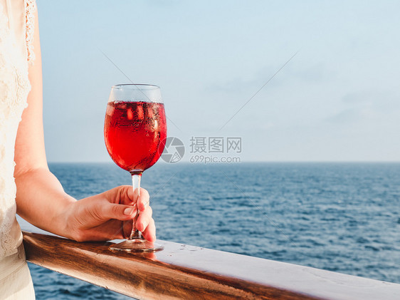 可爱的在蓝色海浪背景下在游轮的露天甲板上拿着一杯漂亮的粉红葡萄酒时尚女人侧视图特写休闲和旅行的概念女人拿着一杯漂亮的粉红葡萄酒鸡图片