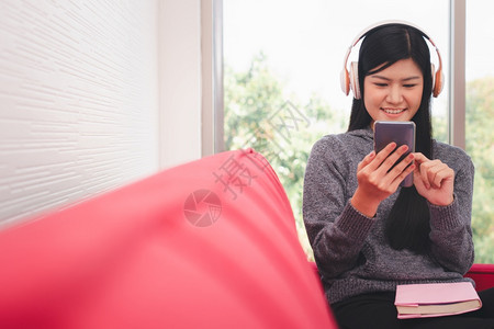 白种人房间技术清晨坐在沙发上的亚洲可爱女人坐在沙发上用手机送信息同时听音乐在客厅大腿上放一本书笑声图片