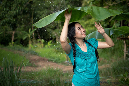 淋浴新鲜的在绿花园背景下雨时一位年轻亚洲女身着香蕉叶的黑头发肖像图片