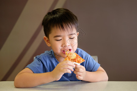 番茄快乐的奶酪亚洲男孩喜欢吃棕色背景的比萨饼图片