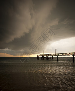 巨大的黑风暴云聚集起来人们在码头上钓鱼场景海滩澳大利亚人图片