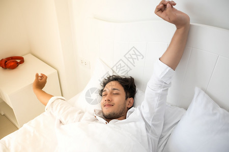 疲劳的女一个男人醒来时躺在床上完全休息早上打开窗帘呼吸新鲜的空气亚洲图片