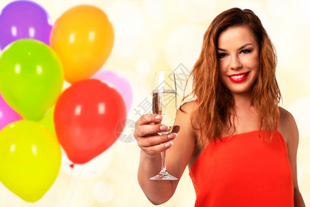 成人吐司庆典祝活动的概念年轻和有魅力的穿红裙子配着完美指甲的红衣妇女拿着一杯香槟或葡萄酒在派对装饰背景上微笑图片