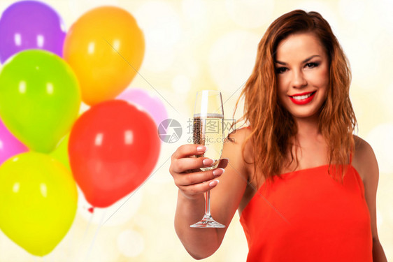 成人吐司庆典祝活动的概念年轻和有魅力的穿红裙子配着完美指甲的红衣妇女拿着一杯香槟或葡萄酒在派对装饰背景上微笑图片