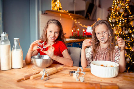 人们魔法孩子在圣诞节上烤姜饼在装饰的客厅里庆祝节日孩子们在装饰的客厅里庆祝快乐小姑娘们在装饰的客厅壁炉做圣诞姜饼屋蜡烛图片