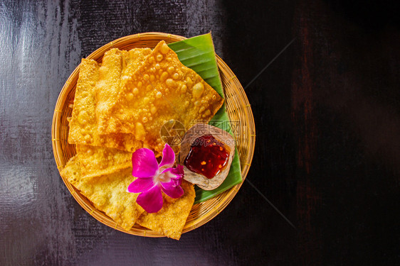 油炸黄色的煎子和竹菜上一碗酱汁装饰用兰花放在桌边的黑木板上重点图片