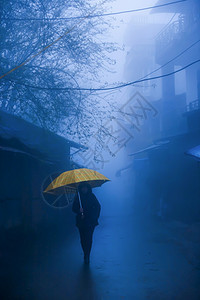步行景观一名身份不明的女穿着雨伞走在古城巷子里身穿黑色夹克的衣单身妇女上手持黄色雨伞行走神秘图片
