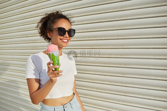 穿着白色T恤和轻牛仔裤的年美籍黑人女孩在日光照耀时用冰淇淋抵挡着一堵轻墙吃冰淇淋甜的天有趣图片