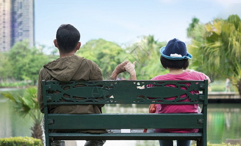 对亚洲夫妇手握坐在公共园区绿色花长椅上分别坐在一起放松和爱的概念反观茶点头发情人图片