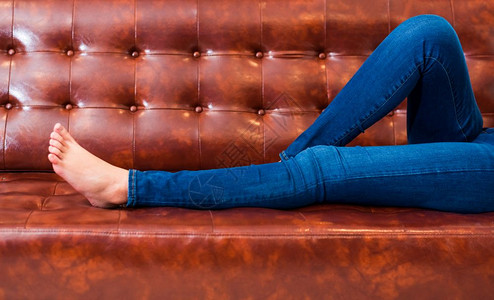 蓝色的女在电影院或家中以棕色皮沙发放松和节假日概念睡觉时间床睡觉人们的生活方式和节假日Clouseup女孩脚剧院腿图片