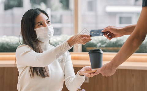 无卡支付戴面具保护和用信卡付咖啡费的亚洲美容妇女生活方式新常态和金融概念新的机器钱背景