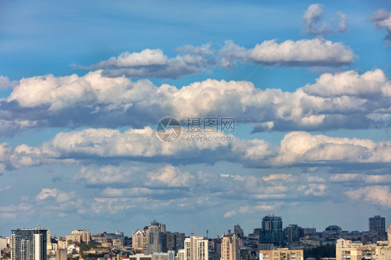 一种天际线城市风景蓝色的天空在城市上徘徊着白云并在太阳光下投阴影复制空间在城市上的蓝色天空中飘浮着大白云和灰城市景观图片