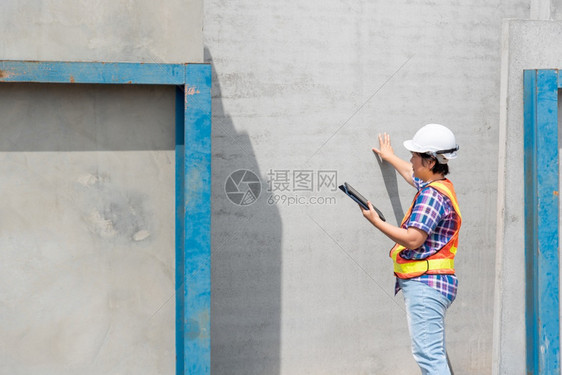 技术建筑学造亚洲女土木建筑工程或设计师身着头盔和安全背心工作并拥有一台触摸不定的平板电脑以查看建筑物或工地的蓝图或计划建筑工地的图片