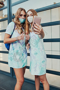 在市中心商店前门站着智能手机的女青年孩用自拍照片身戴面罩以避免感染和防止疾病在科罗纳毒发生时传播的女孩佩戴面罩以防止感染和预防疾图片