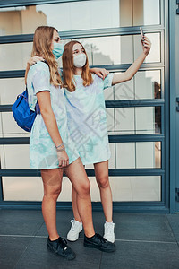健康新冠在市中心商店前门站着智能手机的女青年孩用自拍照片身戴面罩以避免感染和防止疾病在科罗纳毒发生时传播的女孩佩戴面罩以防止感染图片