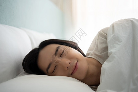 人们快乐的年轻睡得安稳早上在白床做梦假日是快乐笑的亚裔男在家眼闭着的时候躺在舒适软床铺枕头毯子和床垫上年轻的图片