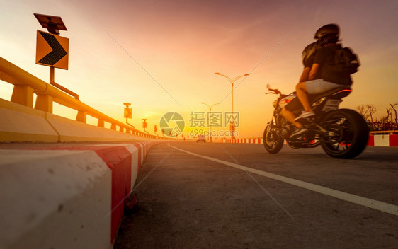 黄曲线交通标志上的太阳能电池板量以及骑摩托车的在弯曲公路上运动模糊夏季假期旅行路上程爱之情夫妇暑假乘摩托车出行家活动发机图片