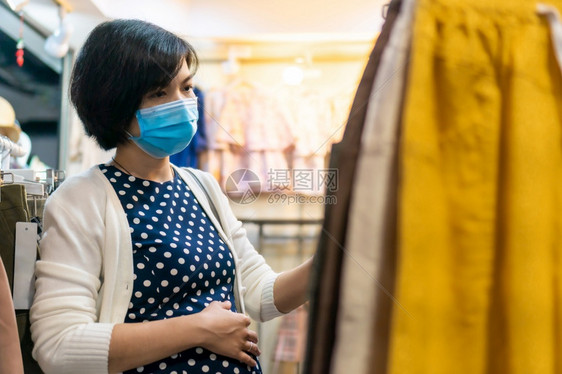 孩子母亚裔孕妇穿着面罩在商店购物年轻女在商店寻找和选择婴儿衣物在商店买服流行病图片