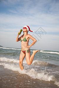 目的地季节圣诞戴帽子的快乐美女在海滩前边跳着舞图片
