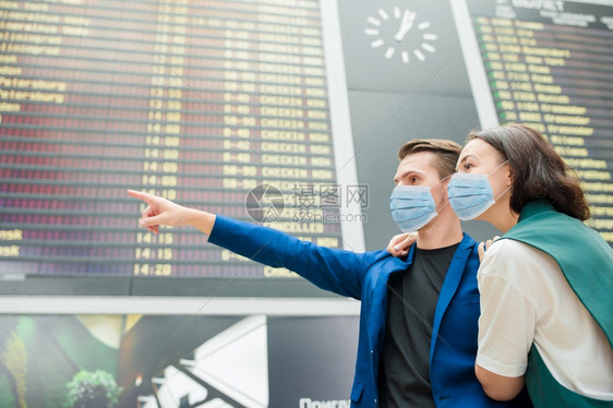商业新冠年轻家庭的肖像在机场保护局的飞行信息板前佩戴防止的面具以对抗科罗纳和国际机场的牵制年轻夫妇们看着飞行信息板注视着飞行信息图片