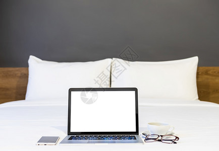 酒店屏幕内部的工作场所在旅馆卧室内背景工作和业余度假期旅行时带空白屏幕的手提式电脑智能手机咖啡杯和眼镜贴在白色床上装饰的品上工作区背景