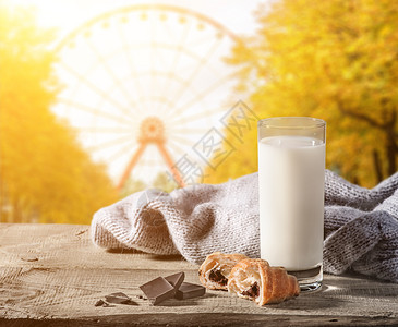 摩天轮秋在公园里一个雪轮的模糊背景牛奶和木桌上的羊角面包在木板上放着一个羊角面包纸一整块巧克力和件毛衣烘烤的面包店图片