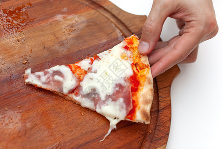 酱熔融人拿了最后一片美味的意大利比萨饼手架握着一块热披萨和火腿一起吃热披萨在白桌上的木板脆图片