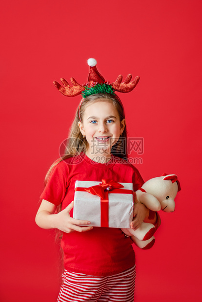拥抱手指广告一个有趣的快乐女孩肖像头上缠着角绷带抱一只泰迪熊穿着圣诞睡衣背景为鲜红色头抱着一只泰迪熊与鲜红色背景隔开图片