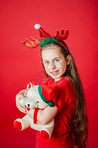 一个有趣的快乐女孩肖像头上缠着角绷带抱一只泰迪熊穿着圣诞睡衣背景为鲜红色头抱着一只泰迪熊与鲜红色背景隔开童年积分玩具图片