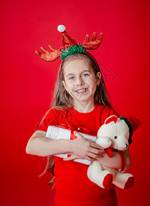 一个有趣的快乐女孩肖像头上缠着角绷带抱一只泰迪熊穿着圣诞睡衣背景为鲜红色头抱着一只泰迪熊与鲜红色背景隔开假期自信的戏服图片