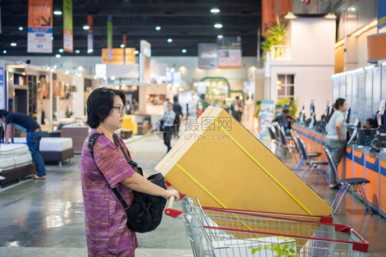 亚裔女在百货店购买大产品时感到快乐在百货商店或展厅览会上买箱装小货车的大产品或者在百货商店买购物车的亚洲女人游客商业的图片