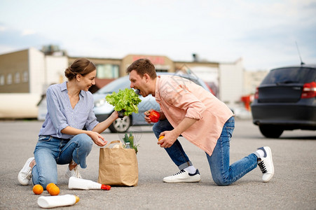 闲暇家庭夫妇在超市的汽车停放上丢下食品包从购物中心买东西的顾客们欢乐快车在背景上的辆在超市停时丢弃了食物包夫妻在超市停车时丢弃了图片