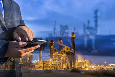 经理过公司商人在夜间用智能电话检查炼油厂工时双倍接触能源与技术概念的双重接触图片