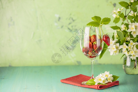 健康新鲜成熟的生草莓红餐巾和绿面纸在色表的葡萄酒杯中盛有绿叶子茶点市场图片