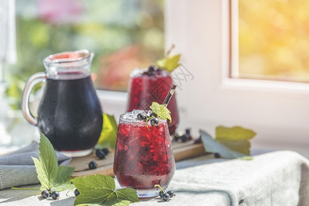 酒精两杯冰冷的黑卷曲兰果汁有成熟的浆果和绿叶子放在窗外有花园的阳光明媚房间桌上清爽喝图片
