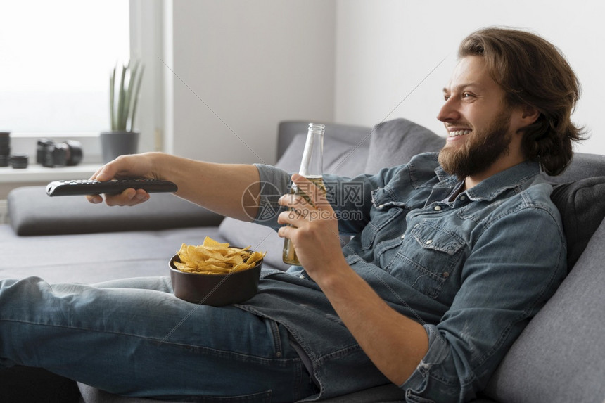 喝着酒拿着零食的男子在沙发上看电视图片