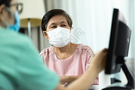 身穿绿色制服的亚洲女医生或护士在院疾病IllFlu生病者Covid19Corona室向穿粉色衣服的老年妇女提供咨询并一起看电脑屏图片