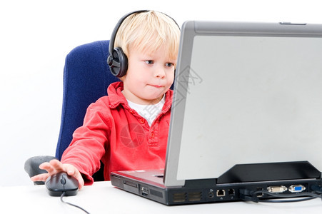 正面坐在笔记本电脑后面的年轻男孩点击计算机mouse同时看着屏幕并戴耳机以及微笑腰部图片