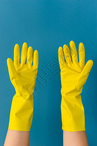 紧贴着身份不明的caucasian女孩的手她用保护黄色橡皮手套举起双用来清洁或消毒在日间对相机的棕榈树上以蓝墙为背景乳胶女士安全图片