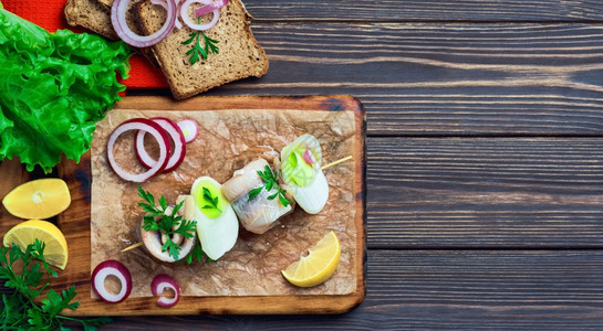 木板复制油鲱鱼卷在烤串上面有欧芹洋葱和柠檬楔子顶视图三明治放在切菜板上深色木质背景上有文字空间图片