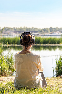 健康瓜拉纳有耳机的女人听柔软音乐在冥想时候早上坐在河前就日出之后清晨坐在河前面图片