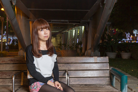 腿坐在棕色公园长椅上看着悲伤的日本女自然绿色图片