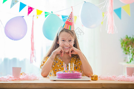 五彩纸屑帽子装饰风格快乐的小女孩在生日蛋糕上吹蜡烛与气球生日晚会一起充满花彩的背景和喜悦生日派对希望概念高加索女孩是梦幻般的微笑图片