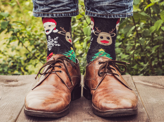 Menrsquos腿穿着时尚的鞋子明亮杂色袜子在绿树背景的木制露台上装饰着圣诞和新年图案美丽时尚优雅腿穿着时尚的鞋子明亮杂色袜子图片