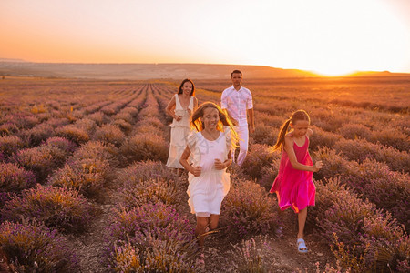 花朵放松紫色的美丽家庭在白衣和帽子日落时在紫花田中的美丽家庭度假图片