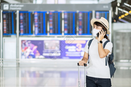 称呼聪明的在机场终端站戴面罩和使用移动智能手机保护科罗纳感染带帽子的新正常亚洲女旅行者以及在COVID19概念下的旅行年轻女妇佩图片