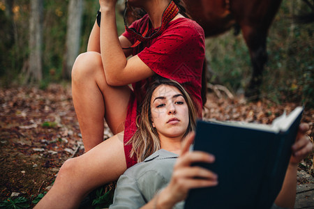 照片春天年轻一对身着洋装的年轻女子正在阅读一本书森林里用旧相机和马拍照微笑图片