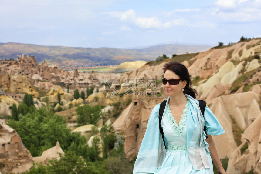 全景卡帕多西亚山谷和峡中洞模糊的景观中一位戴着墨镜件绿松石色连衣裙和肩上背着包的年轻美女肖像卡帕多西亚山谷和峡的模糊景观自然旅行图片