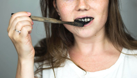 年轻女子用黑色牙膏和活炭刷白色背景上的黑牙刷用于齿美白干净的年轻女子用黑色牙膏和活炭刷白色背景上的黑牙刷用于齿美白卫生保健早晨药图片